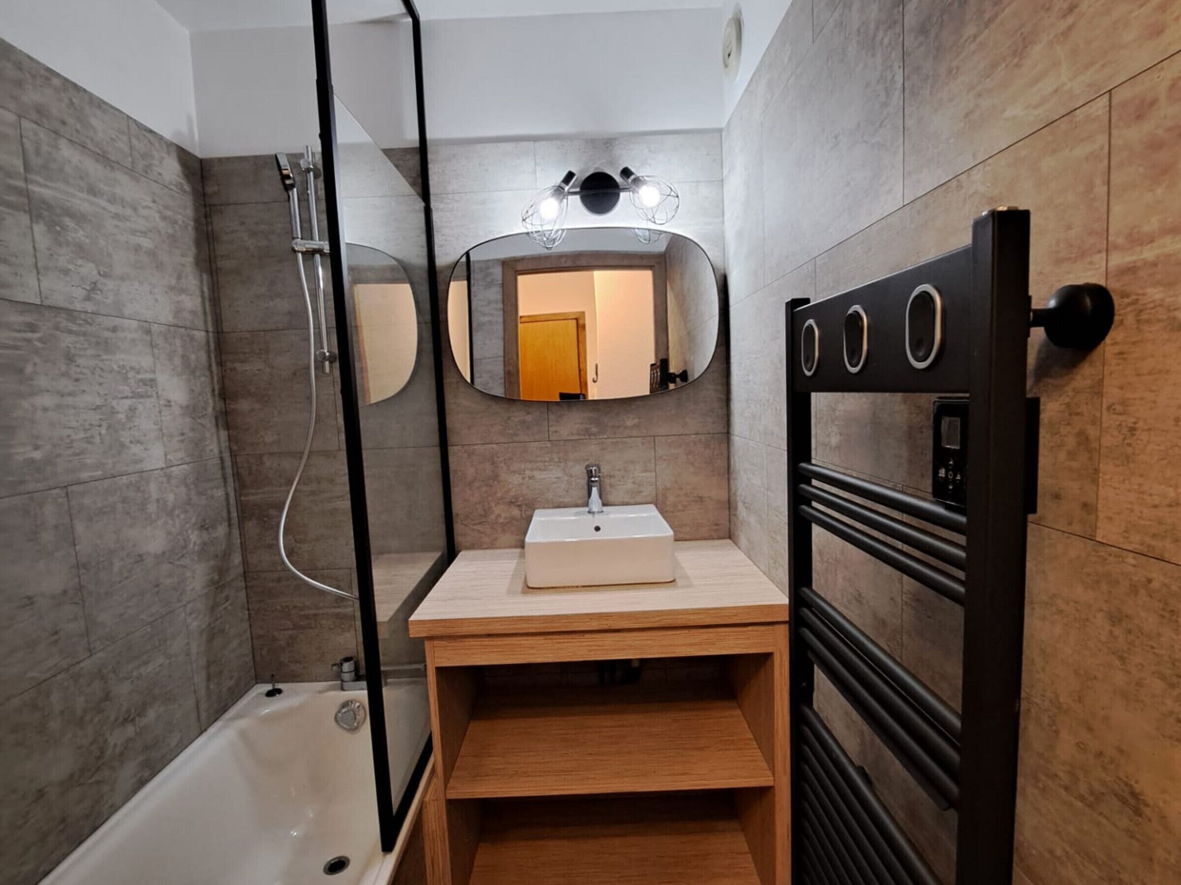 Un baño moderno con bañera, tocador de madera, espejo con iluminación y toallero.