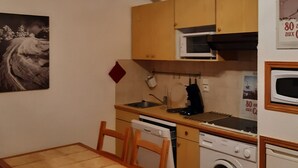 Een kleine keuken met houten kastjes, een magnetron, een spoelbak, een fornuis en een wasmachine.