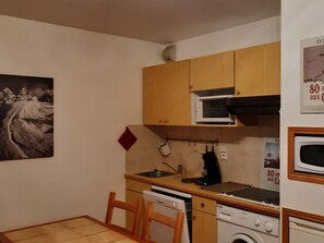 A compact kitchen with wooden cabinets, a microwave, a sink, a stove, and a washing machine. - Cozy Studio with terrace, 4 people, private parking (Arâches-la-Frasse)