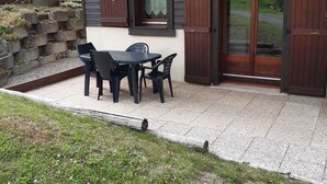 Een terras met een tafel en stoelen, een houten deur en een raam met luiken.