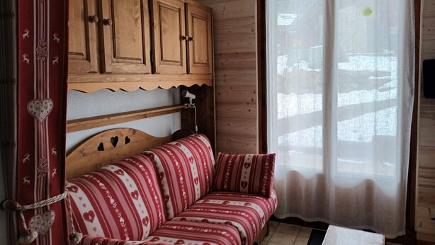Een gezellige kamer met een houten kast, een gestreepte bank en een raam met dunne gordijnen.