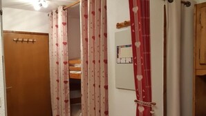 Een kamer met een houten deur, een stapelbed en een rood-gestreepte bank.