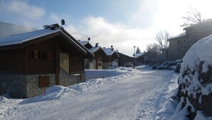 Lumipeitteinen katu, jonka varrella on puutaloja ja kivimuureja, ja taivas on kirkas.