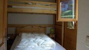 Kerrossänky, jossa on puinen pääty, yhden hengen sänky valkoisella patjalla ja ikkuna, josta avautuu näkymä vehreään maisemaan.