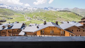 Un chalet de montagne avec des cabanes en bois, une piste de ski et, en arrière-plan, des montagnes enneigées.