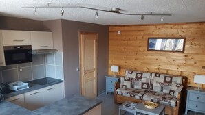 Eine kompakte Küche mit modernen Geräten, einer Holzwand, einem Sofa mit gemustertem Bezug und einem kleinen Tisch mit einem Korb.
