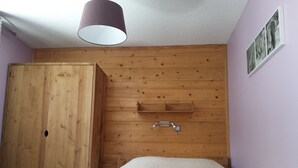 Ein Schlafzimmer mit einem Holzschrank, einem Bett mit weißer Bettdecke und einer Deckenleuchte.