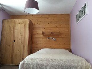Ein Schlafzimmer mit einem Holzschrank, einem Bett mit weißer Bettdecke und einer Deckenleuchte.