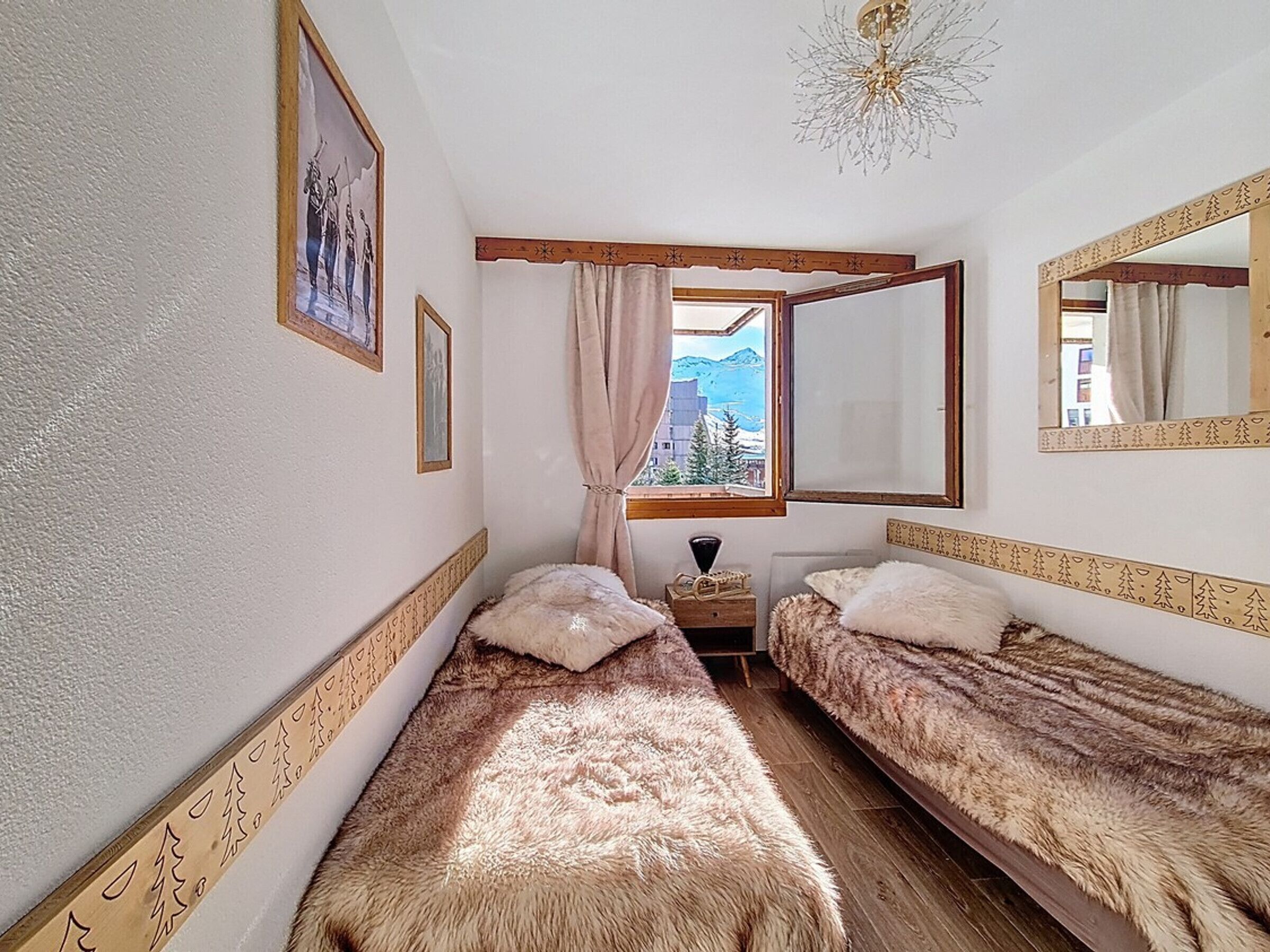A room with two beds, a window with a view of mountains, a mirror, and a chandelier.