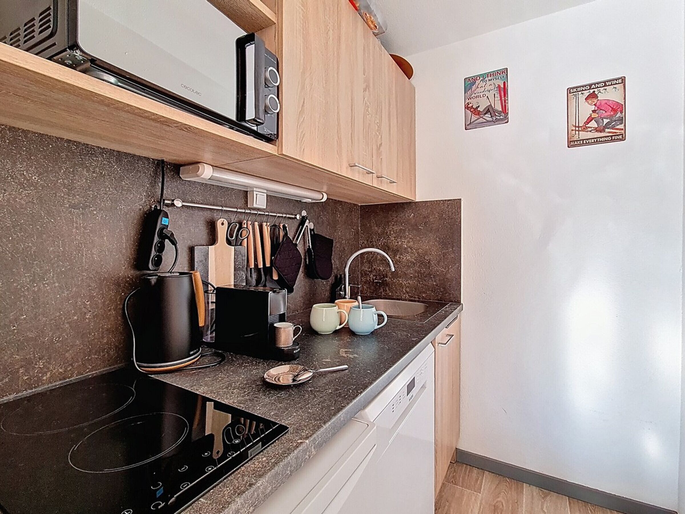 A modern kitchen with a built-in stove, a microwave, and a dishwasher. There are wooden cabinets and a hanging utensil rack.