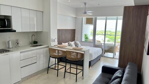 Una cucina moderna con mobili bianchi, un forno a microonde e un lavello. C'è una zona pranzo con tavolo e sedie, e un letto grande con vista sull'esterno.