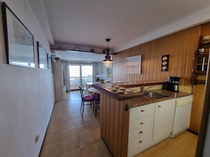 A kitchen with a wooden island, a dining area with chairs, and a view to the outside. - Cozy apartment in L'Escala near the beach (L'Escala)