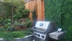 Una parrilla para barbacoa con panel de control y tapa, frente a una cerca de madera y un seto verde.