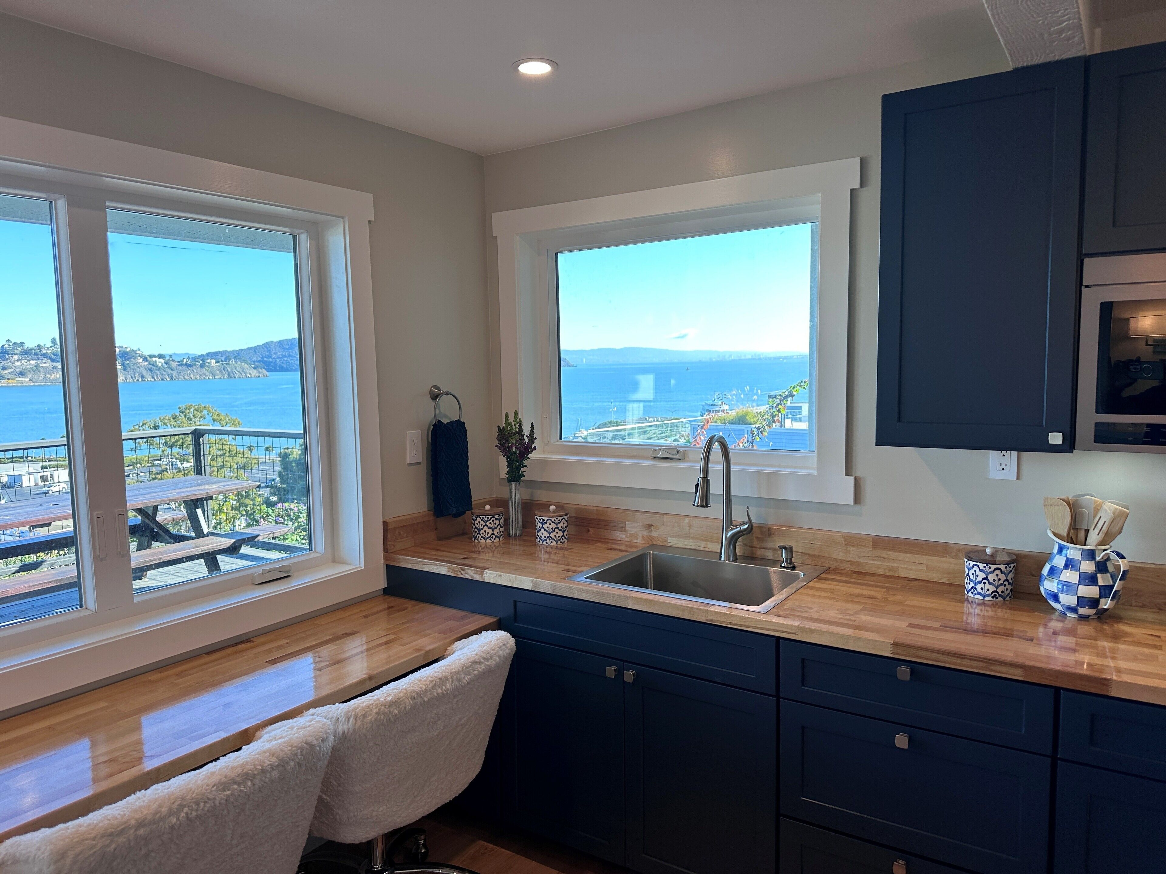 A kitchen with a view of the sea, wooden countertops, and dark blue cabinets.