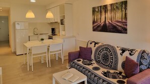 Moderni huoneisto, jossa on pieni keittiö, ruokailutila ja olohuone, jossa on kuviollinen sohva ja metsäteemainen taulu.