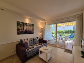 A living room with a sofa, a coffee table, a TV, and a sliding glass door leading to an outdoor patio with a table and chairs. - 1-bedroom apartment with terrace, close to the beach (L'Escala)
