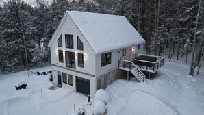 A two-story house with a snow-covered roof, surrounded by trees. - Northview Chalet | Brand New, Hot Tub, Spacious (Conway)