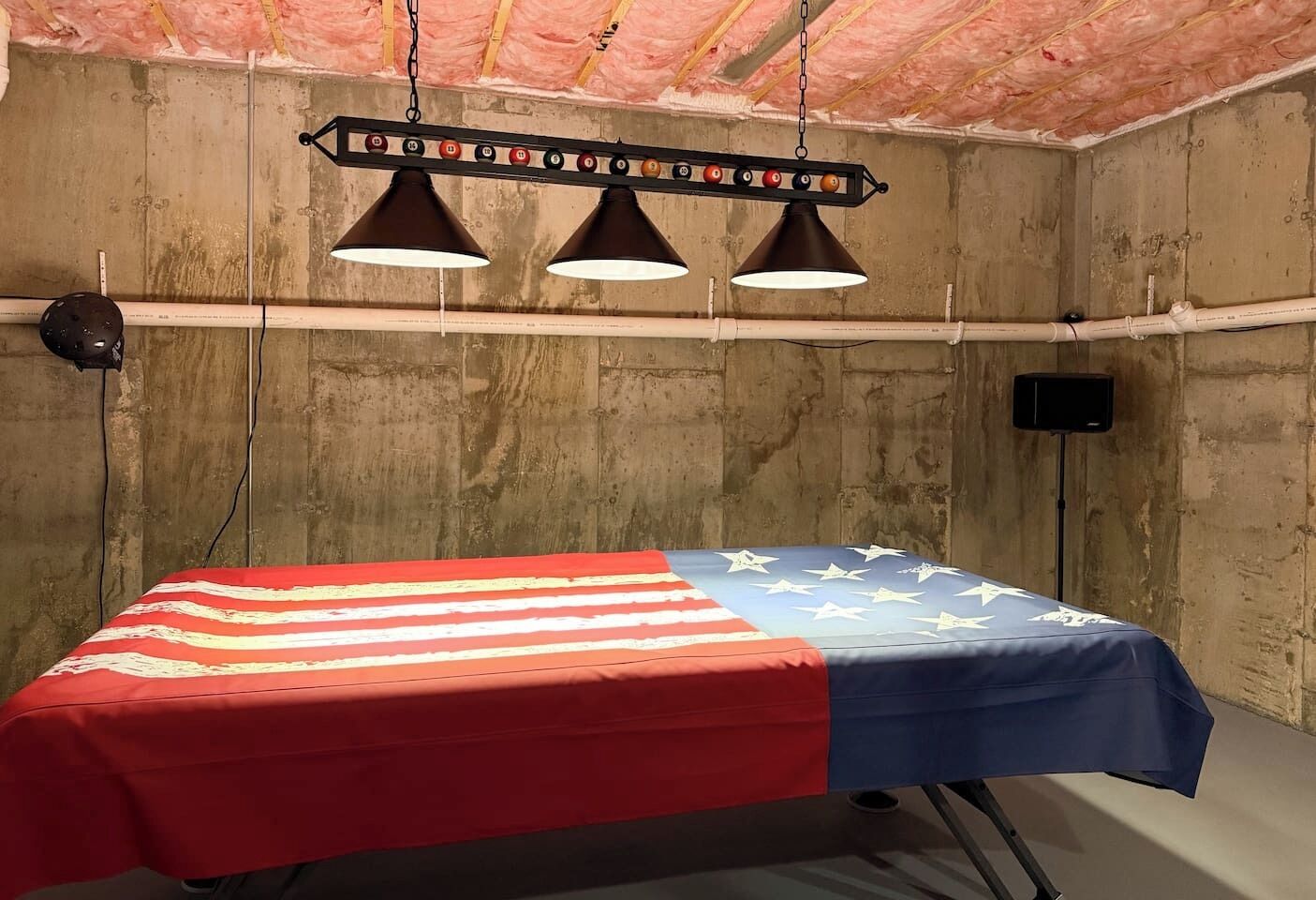 A room with a bed covered in an American flag-themed blanket, a ceiling with insulation, and pendant lights.