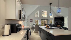 A modern kitchen with a large island, black cabinets, and a fireplace. - Northview Chalet | Brand New, Hot Tub, Spacious (Conway)