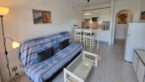 Ein kompakter Wohnbereich mit einer Couch, einem kleinen Couchtisch, einer Küchenzeile und einem Essbereich.