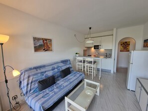Ein kompakter Wohnbereich mit einer Couch, einem kleinen Couchtisch, einer Küchenzeile und einem Essbereich.