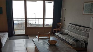 Una habitación pequeña amoblada con sofá, una mesa con una cesta, una silla y un refrigerador.