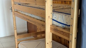 Cama litera con tres niveles, estructura de madera y colchones con correas azules.