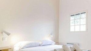 Een minimalistische slaapkamer met een bed, nachtlampen en een raam.