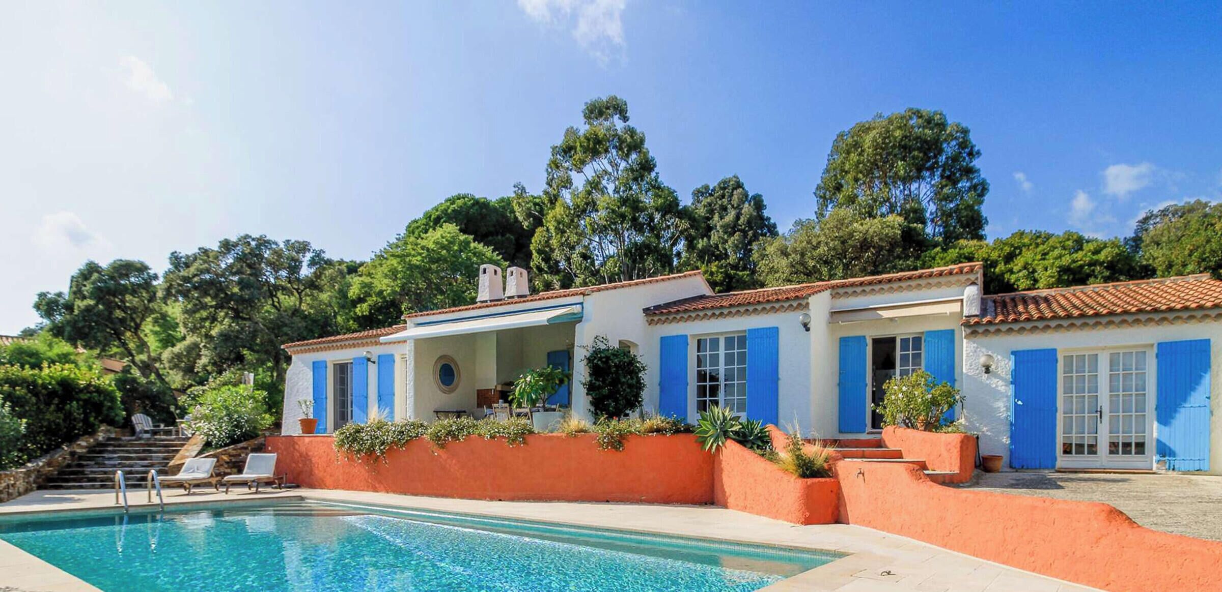 A two-story building with a swimming pool, surrounded by lush greenery and trees.