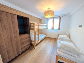 Ein Zimmer mit Etagenbetten, einem Schrank, einem Schreibtisch und einem fenster mit Vorhängen.
