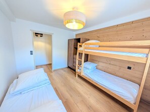 Een kamer met twee stapelbedden, een houten garderobe en een deur naar een andere kamer.