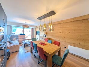 Een modern interieur met een houten eettafel, kleurrijke stoelen, een bank en een keuken.