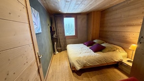 Ein Schlafzimmer mit Holzwänden, einem Bett, einem Fenster, einer Nachttischlampe und einem roten Sessel.