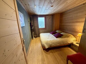 A wooden-paneled bedroom with a bed, a window, a bedside lamp, and a red chair. - Luxury Chalet 5 Bedrooms with Jacuzzi and Parking (Arâches-la-Frasse)