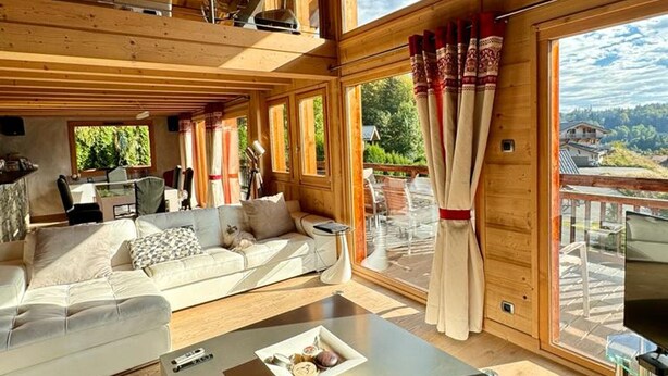 Ein geräumiges Wohnzimmer mit Sofa, Couchtisch und Essbereich. Große Fenster bieten Blick ins Freie.