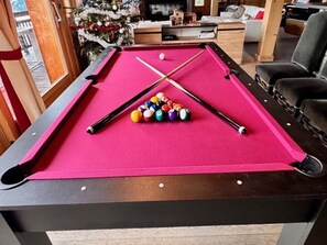 A pool table with a pink felt surface, pool cues, and balls in a room with a Christmas tree and a window. - Luxury Chalet 5 Bedrooms with Jacuzzi and Parking (Arâches-la-Frasse)