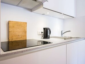Eine moderne Küche mit einer schwarzen Induktionskochplatte, einer Edelstahl-Spüle und einer schwarzen Kaffeemaschine.