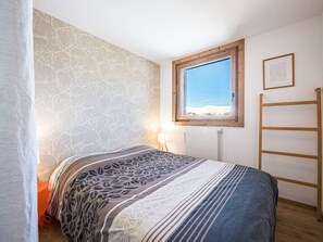 Ein Schlafzimmer mit einem Bett, einem Fenster mit Blick auf Schnee, einer Heizung und einer Holzleiter.