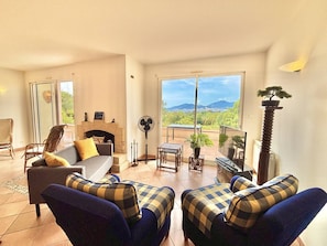 Una sala de estar con chimenea, un sofá, dos sillones, un ventilador y vistas al exterior.
