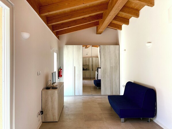 A modern interior with a wooden ceiling, a blue sofa, a wooden cabinet, and a kitchen in the background.