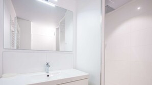 Ein modernes Badezimmer mit einem weißen Waschtisch, einem großen Spiegel und einer Duschkabine.