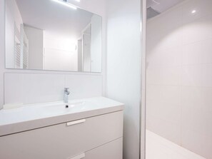 Ein modernes Badezimmer mit einem weißen Waschtisch, einem großen Spiegel und einer Duschkabine.