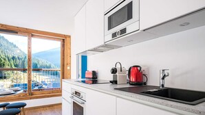 Eine moderne Küche mit einem großen Fenster, einer Spüle, einem Herd und einem roten Wasserkocher.