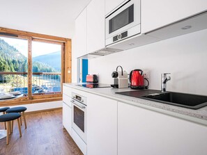 Eine moderne Küche mit einem großen Fenster, einer Spüle, einem Herd und einem roten Wasserkocher.