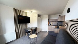 Um espaço compacto para viver com área de jantar, sofá, TV fixada na parede e uma kitchenette.