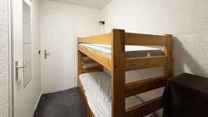 Quarto pequeno com uma cama beliche de madeira, uma porta e uma pequena mesa.