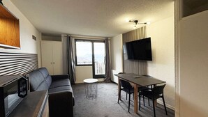 Quarto de hotel moderno com sofá, uma mesinha, televisão fixada na parede e varanda com vista.