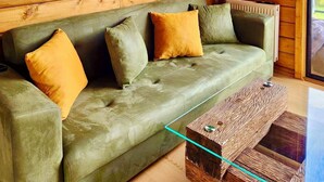Ein gemütliches Holzhaus-Interieur mit einem grünen Sofa, einem rustikalen Couchtisch und einem Fenster mit Blick auf viel Grün.