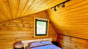 Ein gemütliches Schlafzimmer in einer Holzhütte mit einem Einzelbett, einem kleinen Nachttisch, einem Fenster und einer Holzleiter.