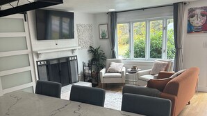 Ein modernes Wohnzimmer mit einem Marmorestisch, Sofas, einem Kamin und großen Fenstern mit Blick auf Grünflächen.